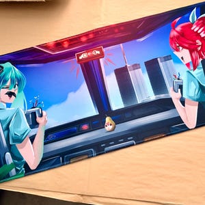 Op de afbeelding: Een rechthoekige muismat met een illustratie in anime-stijl. Het ontwerp bevat twee vrouwelijke personages met kleurrijk haar, tegen een achtergrond van een stadsgezicht en een blauwe lucht. De muismat is voornamelijk blauw en zwart.