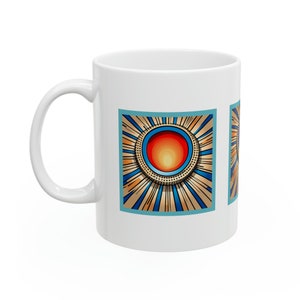 Puede incluir: Taza de cerámica blanca con un diseño de sol estilizado. La obra de arte incluye un círculo central rojo y amarillo rodeado de líneas doradas y azules radiantes, dentro de un cuadrado turquesa. La taza tiene un asa curvada.