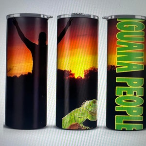 May include: Three stainless steel tumblers with different designs. The first tumbler features a silhouette of a person with their arms raised against a sunset background. The second tumbler features a green iguana against a sunset background. The third tumbler has the text "IGUANA PEOPLE" in green letters on a black background.