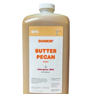 May include: A large, rectangular bottle of Dunkin' Butter Pecan Swirl. The bottle is filled with a light brown liquid and has a white cap. The label features the Dunkin' logo and the words "Butter Pecan" in orange. The bottle contains 64 fl oz.