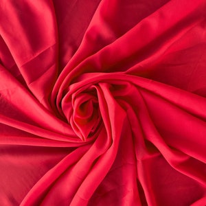 May include: A close-up of a bright red fabric draped and folded into a swirl pattern. The fabric is smooth and silky.