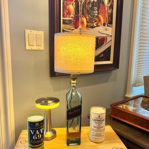 May include: A wooden table with three bottles, two of which are lit with candles. The bottles are labeled "Vat 69", "Blue Label", and "Laphroaig 27". The table has a signature on it that says "Guest Book".