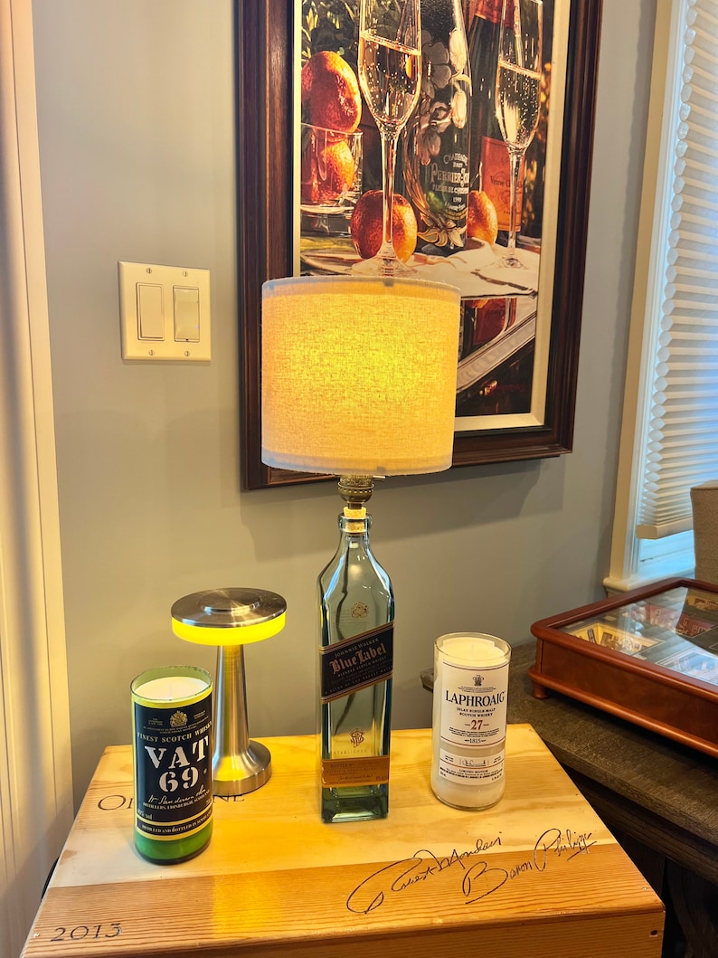 May include: A wooden table with three bottles, two of which are lit with candles. The bottles are labeled "Vat 69", "Blue Label", and "Laphroaig 27". The table has a signature on it that says "Guest Book".