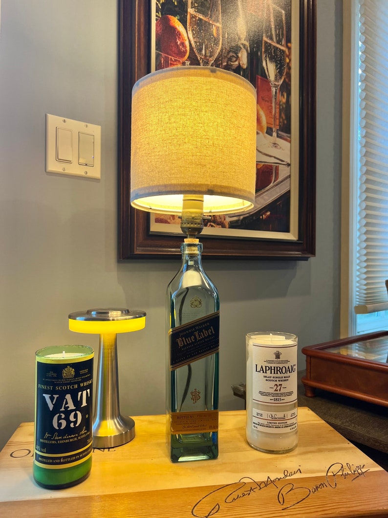 May include: A wooden table with three candles made from repurposed liquor bottles. The candles are labeled "Vat 69", "Blue Label", and "Laphroaig 27".