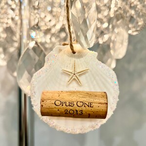 May include: A white seashell ornament with a starfish and a wine cork with the text "Opus One 2013".