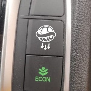 May include: A black car dashboard with two buttons. The top button has a white graphic of a tyre with arrows pointing down. The bottom button is green and has the word "ECON" written on it.