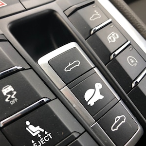 May include: Close-up of a car's dashboard with several buttons. The buttons have various symbols, including a car, a turtle, and a seat with an eject button. The buttons are black with silver trim.