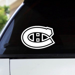 May include: White vinyl decal of the Montreal Canadiens hockey team logo. The logo is a stylised "C" with a horizontal line through the centre and two smaller circles on either side of the line.