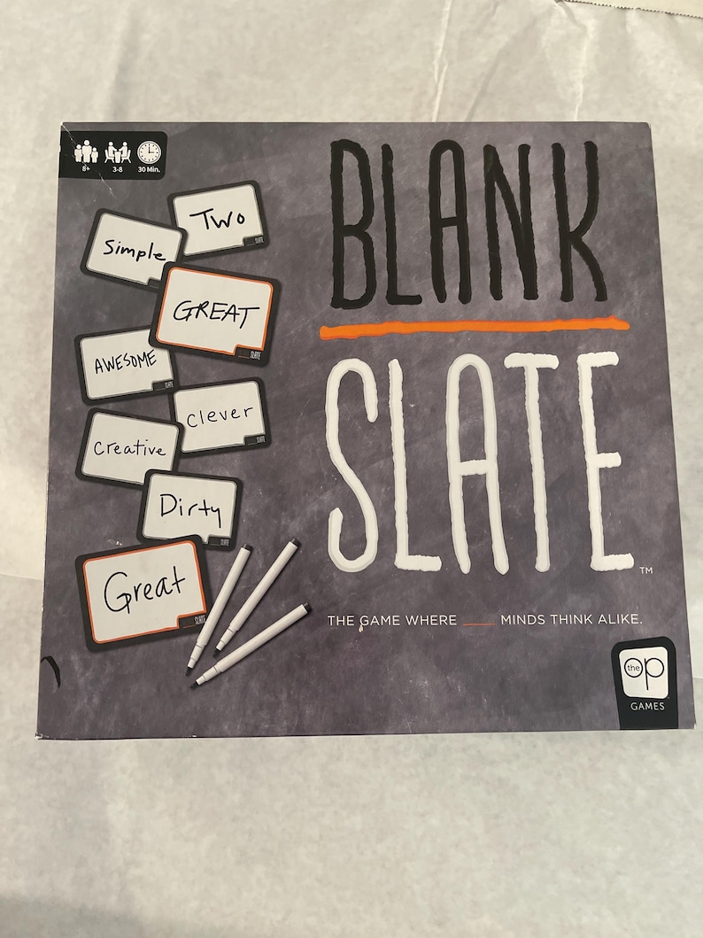 Puede incluir: Una caja de juego de mesa titulada "BLANK SLATE" con texto blanco y una l&iacute;nea naranja. La caja presenta peque&ntilde;as pizarras con palabras como "Simple" y "Great", junto con marcadores blancos. El juego es de "op GAMES".