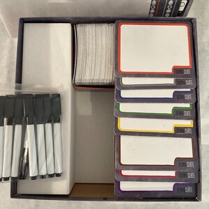Puede incluir: Caja de juego abierta con componentes. Incluye una pila de tarjetas en blanco con bordes de colores, un juego de marcadores negros y un tablero de juego. Las tarjetas est&aacute;n etiquetadas como "BLANK SLATE". La tapa de la caja dice "GAME RULES".