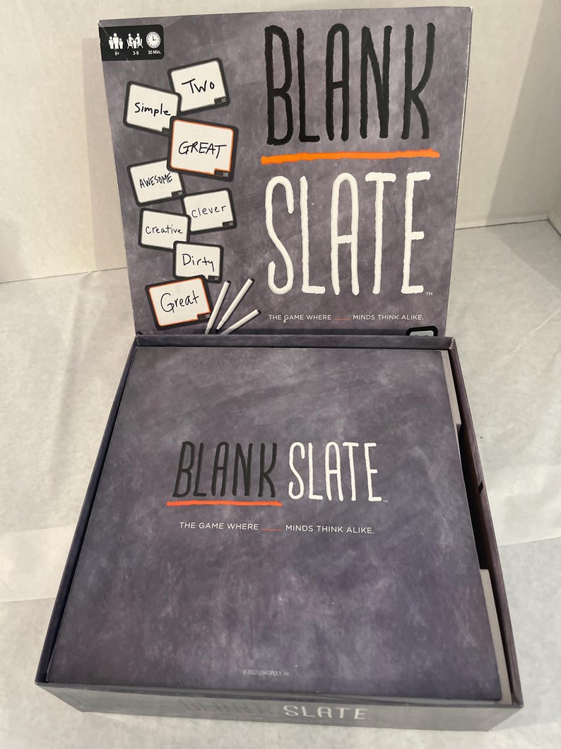 Puede incluir: Caja de juego de mesa abierta, gris, con el t&iacute;tulo "BLANK SLATE" en letras blancas. El juego incluye tarjetas con palabras como "Simple", "Awesome" y "Creative". El juego est&aacute; dise&ntilde;ado para 3-8 jugadores.