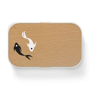 Op de afbeelding: Rechthoekige lunchbox met een witte rand en een houten deksel. Het deksel heeft een lichtbruin houtnerfpatroon en een zwart-wit koi-visontwerp. De vissen zijn gestileerd en kijken elkaar aan.