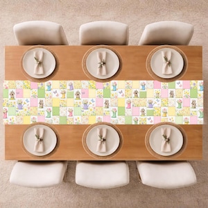 May include: A wooden dining table set for six, viewed from above. Each place setting has a white plate, a beige napkin, and a woven placemat. A colourful patchwork table runner with floral and garden-themed squares runs down the centre.