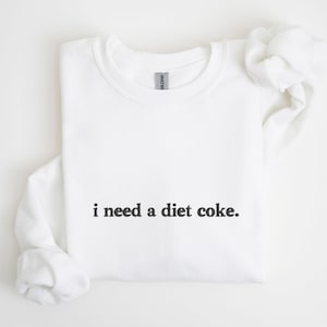 Puede incluir: Sudadera blanca con el texto "i need a diet coke." impreso en negro.