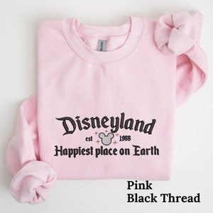 May include: Pink sweatshirt with black text that reads "Disneyland est. 1955 Happiest place on Earth" with a black and white Mickey Mouse head graphic.