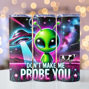 May include: A set of three stainless steel tumblers with a space-themed design. The tumblers feature a green alien with big eyes, a flying saucer, a cow, and the text "Don't make me probe you". The background is a dark blue with stars and a galaxy.
