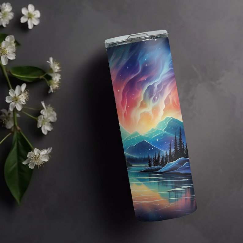 Puede incluir: Un vaso de acero inoxidable con una escena de monta&ntilde;a colorida y un reflejo del cielo en el agua. La escena presenta una cordillera con un lago en primer plano y un cielo colorido con estrellas y nubes.
