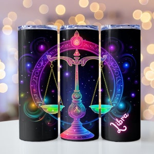 May include: Three stainless steel tumblers with a black background and a colorful neon design of the Libra zodiac symbol. The symbol is a set of scales with a star-filled background. The word "Libra" is written in neon pink on the right tumbler.