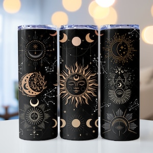 Könnte beinhalten: Drei schwarze Edelstahlbecher mit goldenen Himmelsmotiven. Die Designs beinhalten Monde, Sterne und eine Sonne mit einem Gesicht.