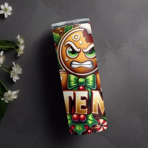 May include: A stainless steel tumbler with a festive gingerbread man design. The gingerbread man has an angry expression, green eyes, and a green bow tie. The word "TEN" is displayed in gold letters, surrounded by holly and candy canes.