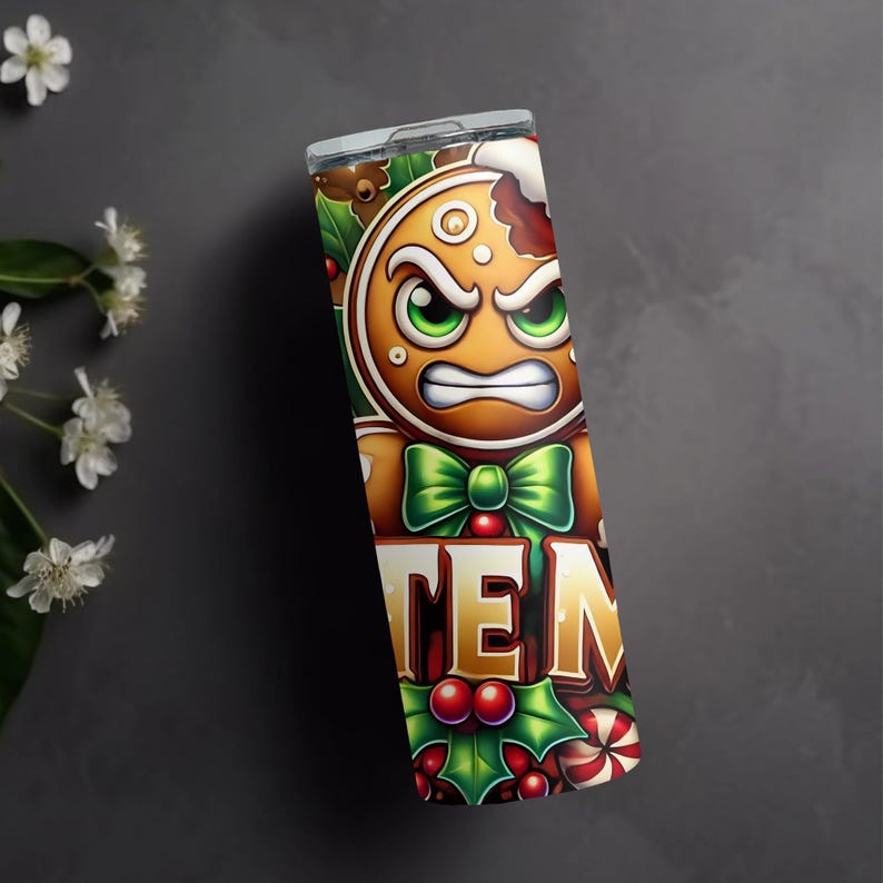 May include: A stainless steel tumbler with a festive gingerbread man design. The gingerbread man has an angry expression, green eyes, and a green bow tie. The word "TEN" is displayed in gold letters, surrounded by holly and candy canes.
