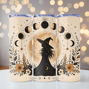 May include: A beige tumbler featuring a witch silhouette in a black dress and hat, set against a full moon. The design includes phases of the moon, stars, and floral accents in brown and gold. The tumbler has a clear lid.