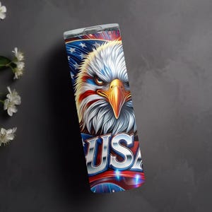 May include: A stainless steel tumbler with a patriotic design featuring a bald eagle with red, white, and blue feathers, and the word "USA" in a metallic font.