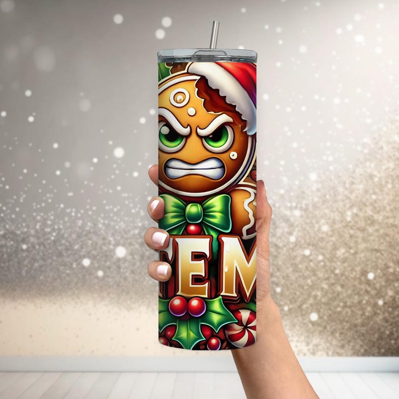 May include: A stainless steel tumbler featuring a cartoon gingerbread man with an angry expression, wearing a Santa hat. The tumbler has a green bow, holly, and the letters "EM". It includes a silver straw and a lid.