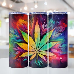 Puede incluir: Tres vasos de acero inoxidable con un diseño abstracto colorido que presenta una gran hoja de marihuana verde. El diseño es una mezcla de rojo, naranja, amarillo, verde, azul y morado.