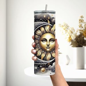 Puede incluir: Un vaso de acero inoxidable con un dise&ntilde;o negro y dorado que presenta un sol y una luna con estrellas y nubes.