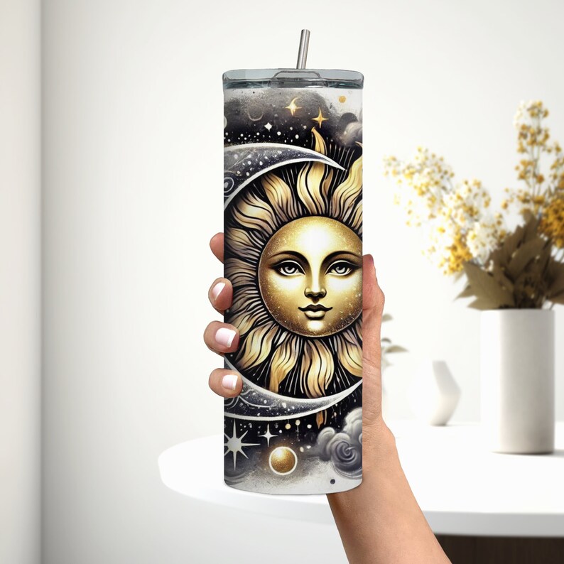 Puede incluir: Un vaso de acero inoxidable con un dise&ntilde;o negro y dorado que presenta un sol y una luna con estrellas y nubes.