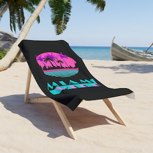 Könnte beinhalten: Ein schwarzes Strandtuch mit einer Retro-Grafik von Palmen und einem Sonnenuntergang. Der Text "Miami Vice" ist in Blau und Pink gedruckt.
