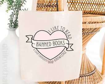 May include: A white canvas tote bag with a pink heart design that says "I like to read banned books & gain forbidden knowledge".