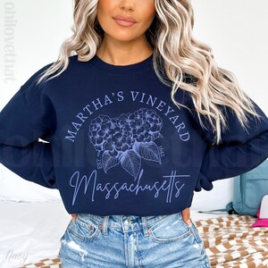 May include: A navy blue sweatshirt with a white graphic design that says "Martha's Vineyard Est. 1642 Massachusetts". The graphic also features a blue floral design.