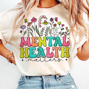 May include: A white t-shirt with a colorful graphic design featuring flowers and the text "MENTAL HEALTH matters".