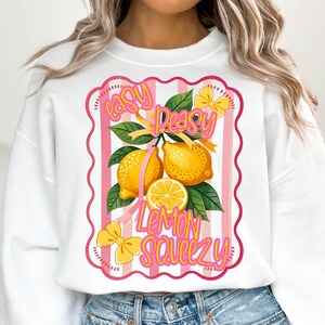 Peut inclure: Sweat-shirt blanc avec un motif ray&eacute; rose et blanc repr&eacute;sentant des citrons et le texte "easy peasy lemon squeezy".