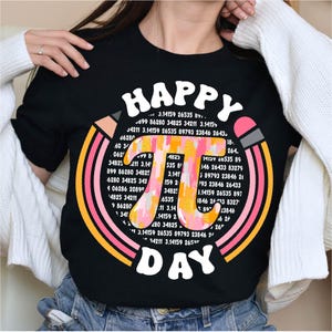 May include: A black t-shirt with a colorful graphic design featuring the mathematical constant pi, surrounded by rainbow-colored stripes and the text "Happy Pi Day".