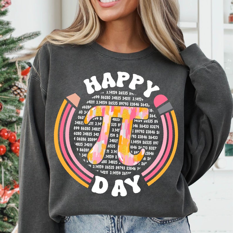 May include: A dark grey sweatshirt with a pink and orange rainbow design and the text "HAPPY PI DAY" in a retro font. The rainbow design includes the number pi (&pi;) with a series of digits.