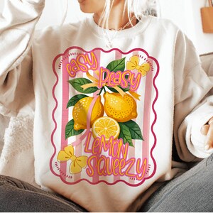 Peut inclure: Sweat-shirt blanc avec un motif ray&eacute; rose et blanc repr&eacute;sentant des citrons et le texte "easy peasy lemon squeezy".