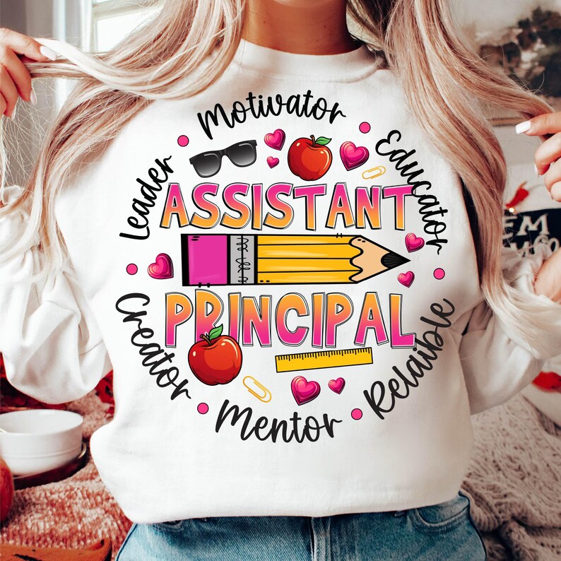 May include: White sweatshirt with a colorful graphic design. The design features the words "Assistant Principal" and other words like "Motivator" and "Educator" in a circular pattern, along with a pencil, hearts, and an apple.