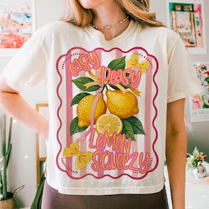 Peut inclure: Un t-shirt blanc avec un motif &agrave; rayures roses et blanches repr&eacute;sentant des citrons et le texte "easy peasy lemon squeezy".