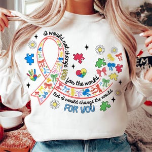 May include: White sweatshirt with a colorful ribbon and puzzle pieces. The text reads "I would not change you for the world, but I would change the world for you."