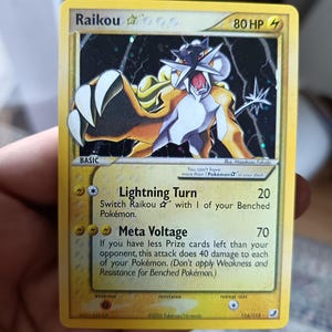 Puede incluir: Una carta coleccionable Raikou Gold Star con borde amarillo, 80 HP y los ataques Lightning Turn y Meta Voltage. La carta muestra una ilustración del personaje Raikou amarillo y negro sobre un fondo oscuro y estrellado.