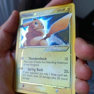 Op de afbeelding: Een gele Pikachu Gold Star ruilkaart met 60 HP, met een illustratie van Pikachu die een groot zwaard vasthoudt. De kaarttekst bevat de aanvallen Thundershock en Spring Back, met het copyright 2006 Pokémon/Nintendo onderaan.