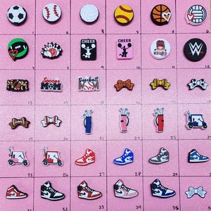 May include: A collection of 36 colorful shoe charms featuring various sports, activities, and designs.  The charms include a soccer ball, baseball, volleyball, basketball, a golf bag, a golf cart, a bow, a football, a bowling pin, a cheerleading pom-pom, a wrestling logo, and a shoe.  The charms are made of a variety of materials, including plastic, rubber, and metal.
