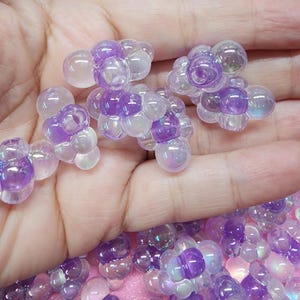 May include: A group of iridescent purple and white bubble beads. The beads are clustered together and have a translucent appearance.