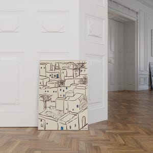 Pu&ograve; includere: Una stampa artistica raffigurante un paesaggio urbano stilizzato con edifici beige, contorni neri e accenti di finestre blu. Anche le palme sono incluse nell'illustrazione. L'opera d'arte &egrave; esposta su un muro bianco.