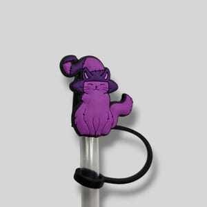 May include: A purple cat-shaped straw topper wearing a witch hat. The cat is sitting and has a raised paw. The straw is clear with a black silicone ring and a black loop.