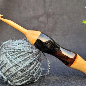 May include: A wooden crochet hook with a black and brown stained handle. The hook is resting on a ball of blue yarn.