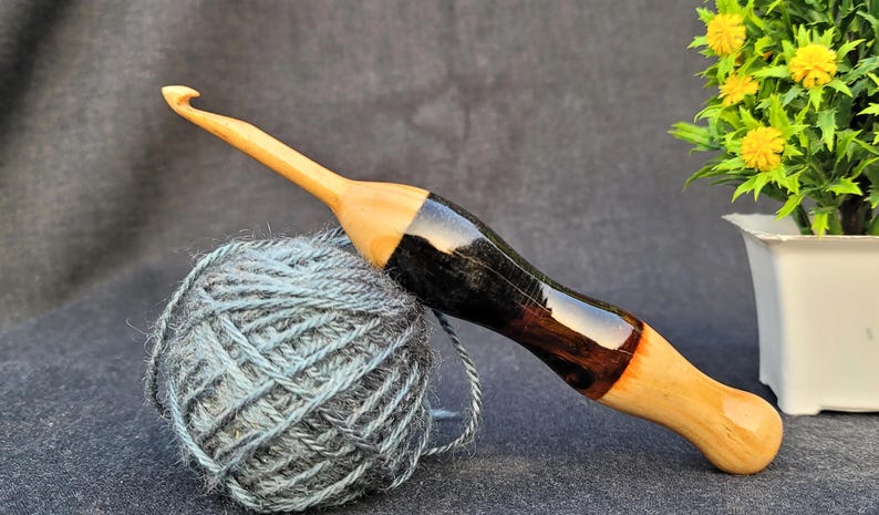 May include: A wooden crochet hook with a black and brown stained handle. The hook is resting on a ball of blue yarn.